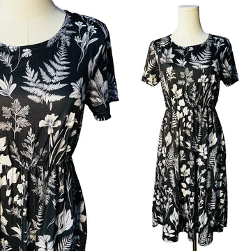 Two black dresses with white floral and leaf patterns on mannequins against a white background.